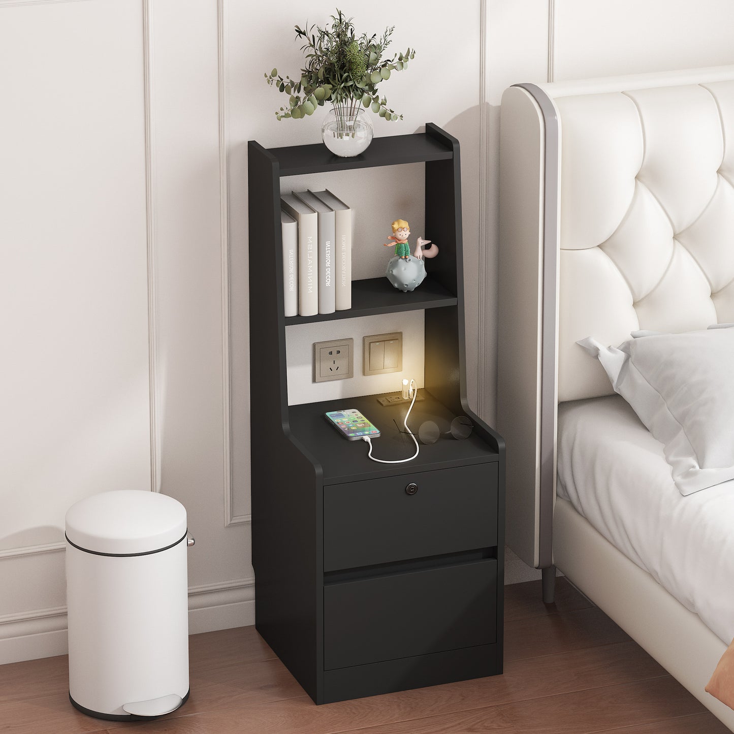 Black nightstand with drawer, books, and a plant next to a bed in a bedroom.