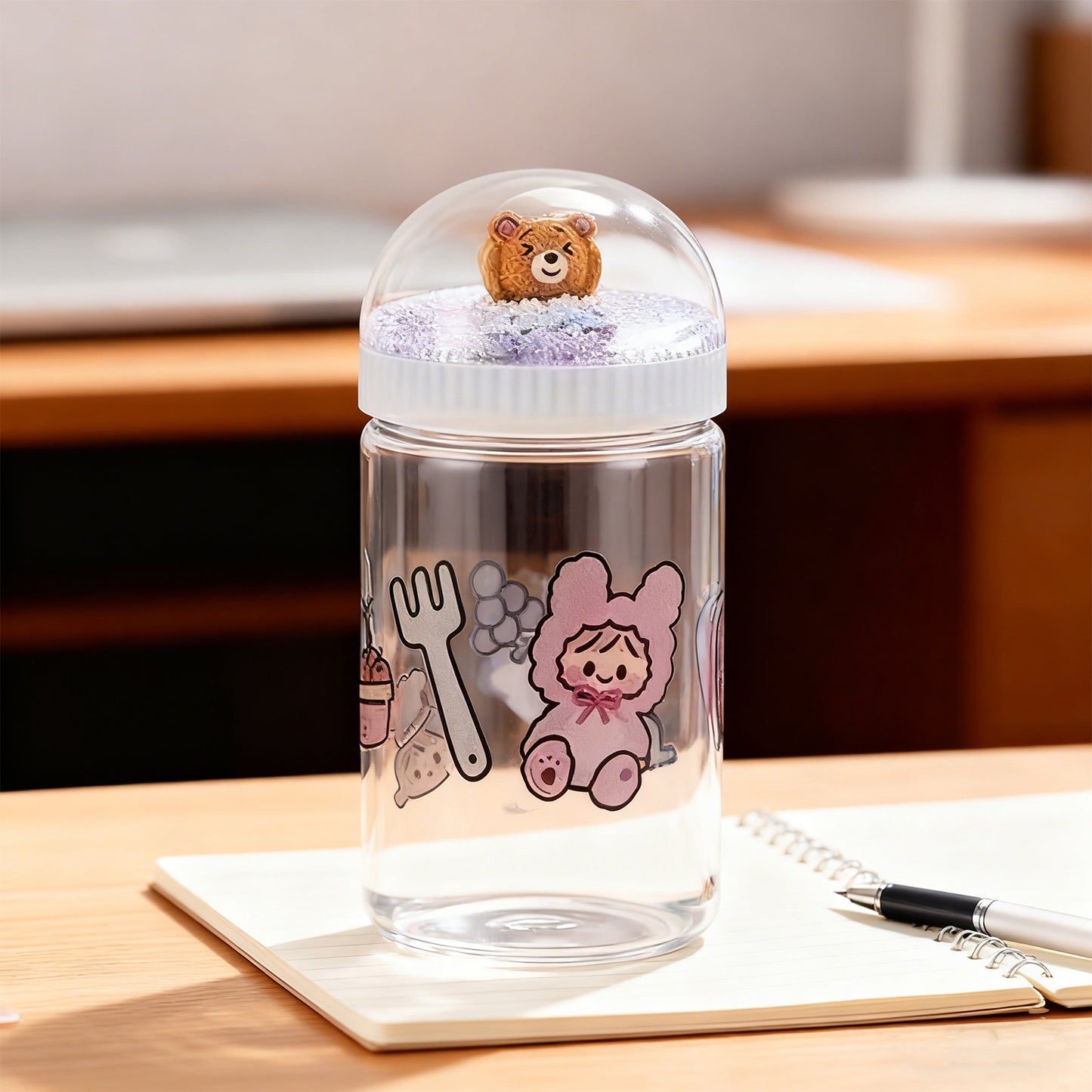 Clear water bottle with cartoon characters and a small bear toy on a desk.