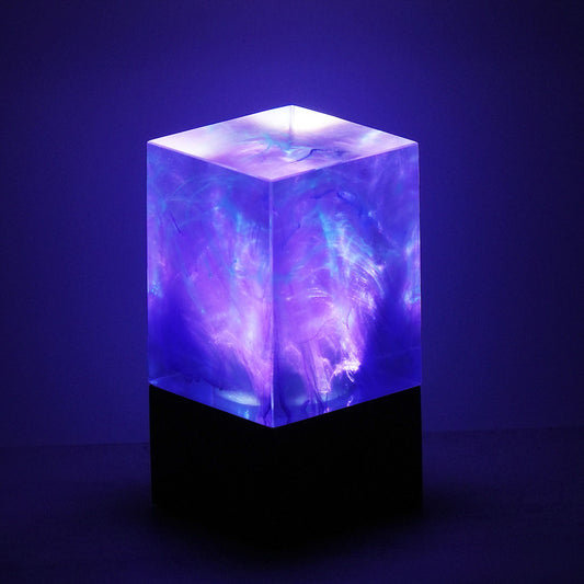 Cube-shaped lamp with swirling purple and blue light on a dark background