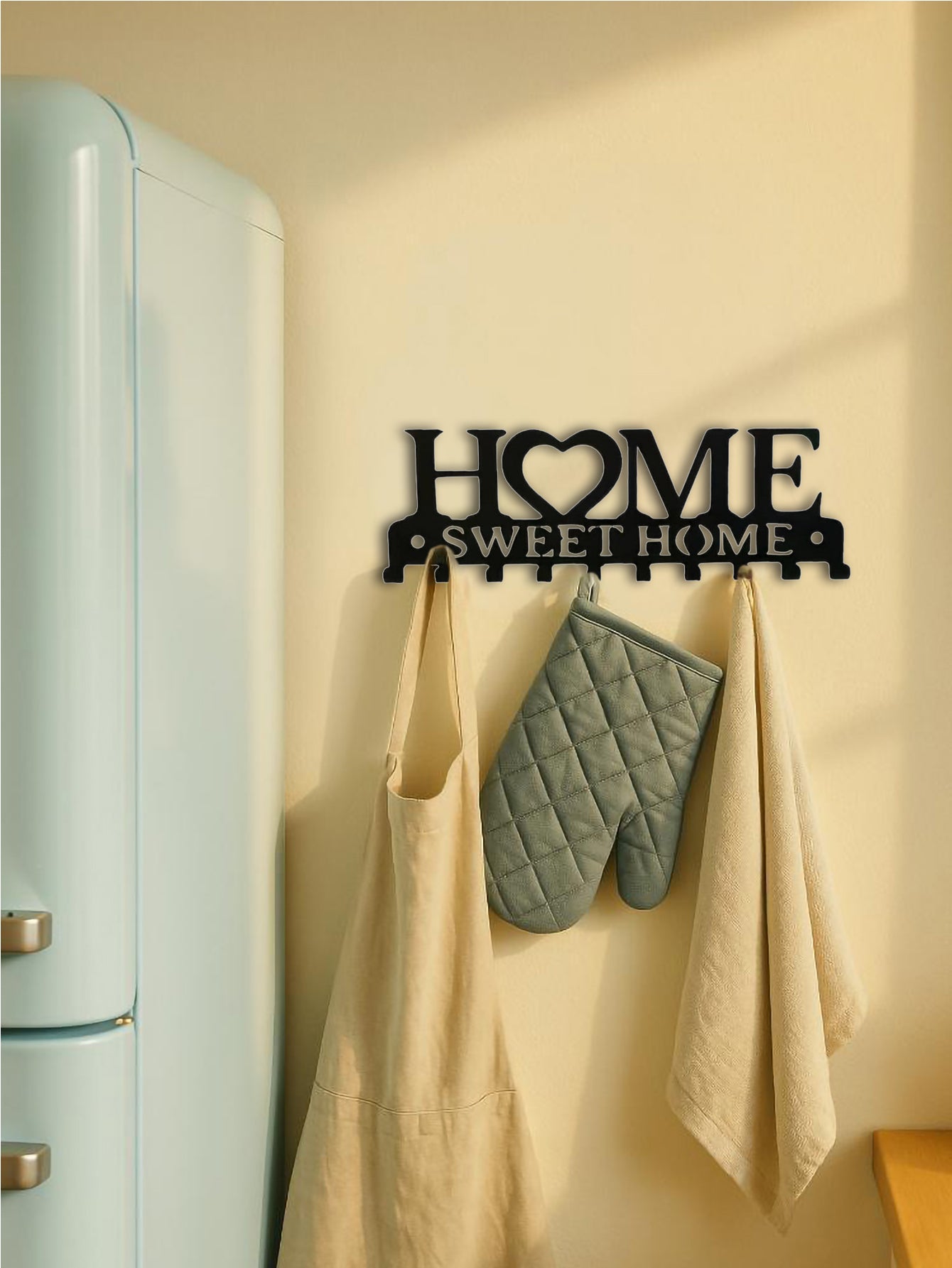 Decorative wall art with 'Home Sweet Home' on a kitchen wall with apron, oven mitt, and towel.