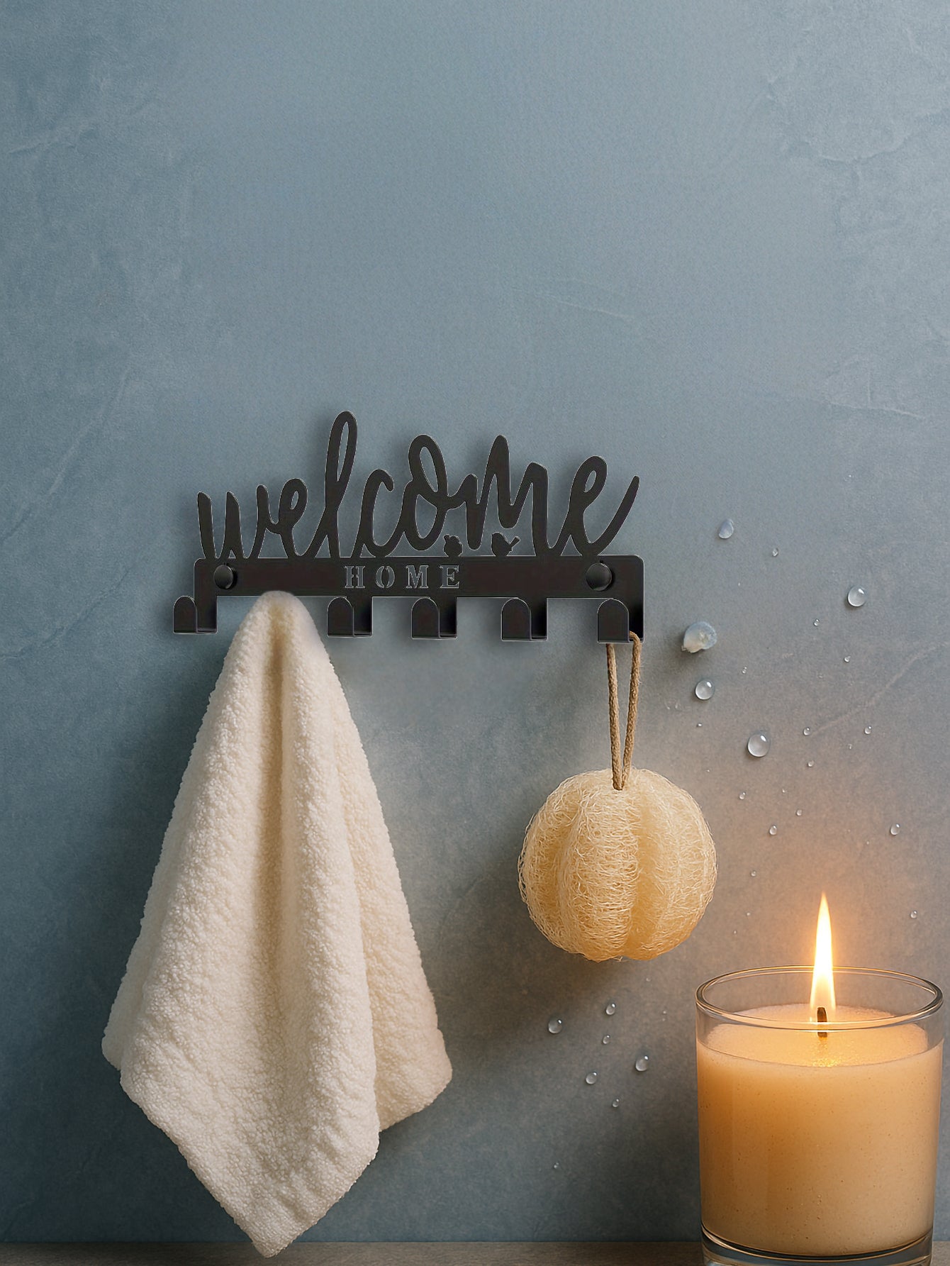 Decorative wall hook with 'welcome home' text, towel, and candle on a textured wall.