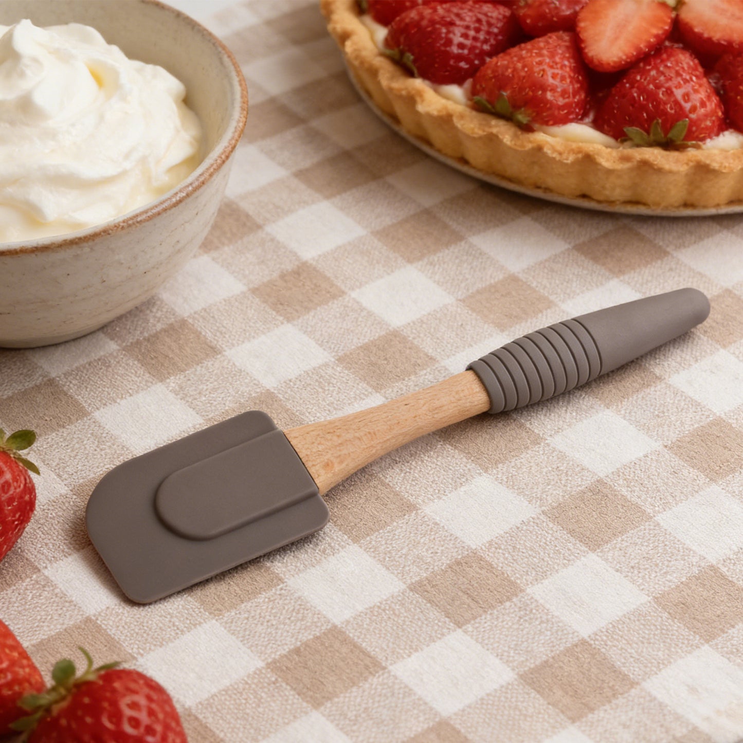 Gray spatula with wooden handle on a checkered tablecloth with strawberries and cream.
