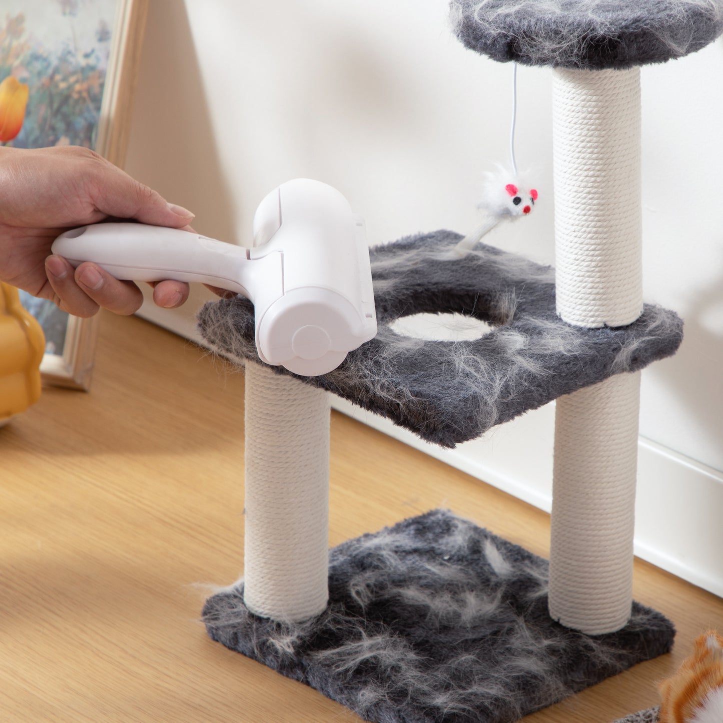 Person using a pet grooming tool on a cat tree with fur collected on it.