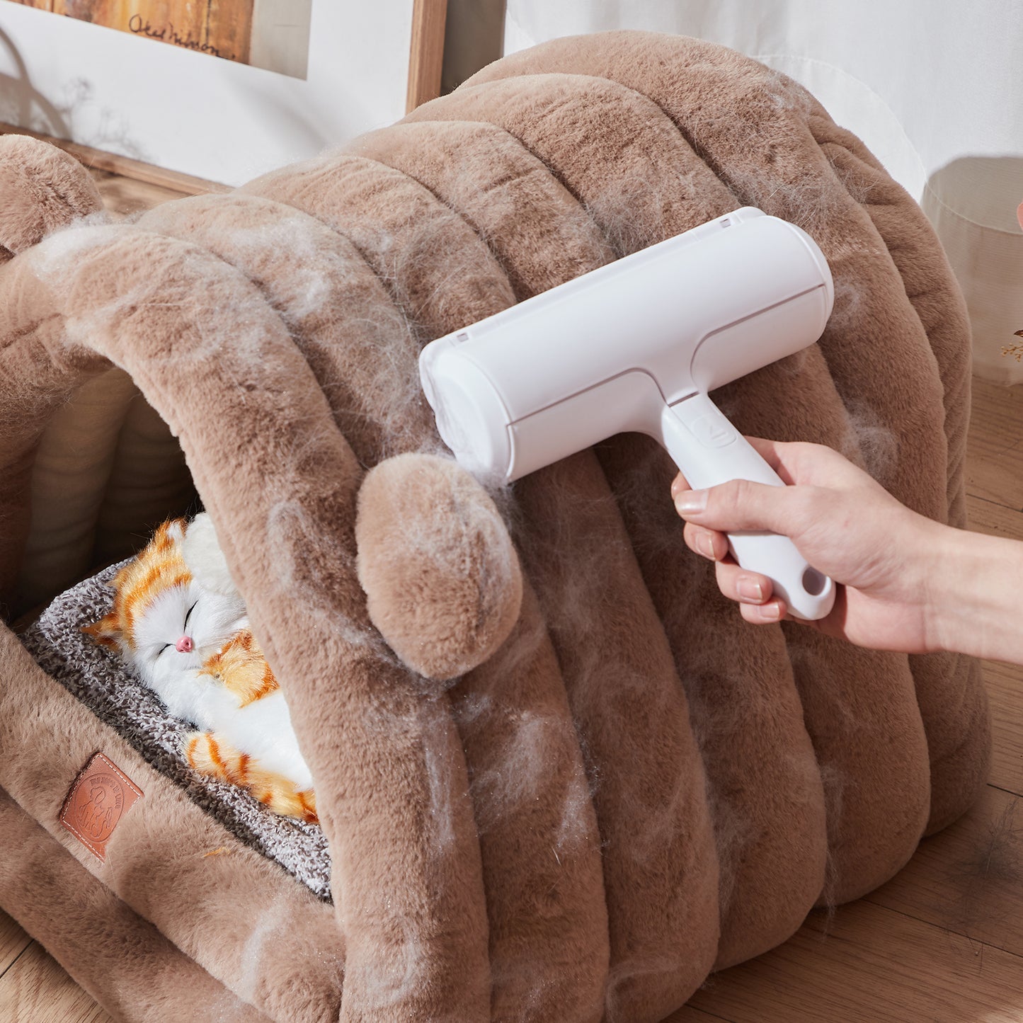 Person using a white pet grooming tool on a fluffy brown blanket with a cat underneath.