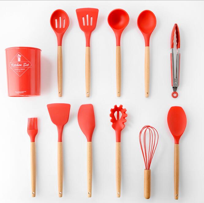 Set of red silicone kitchen utensils with wooden handles on a white background