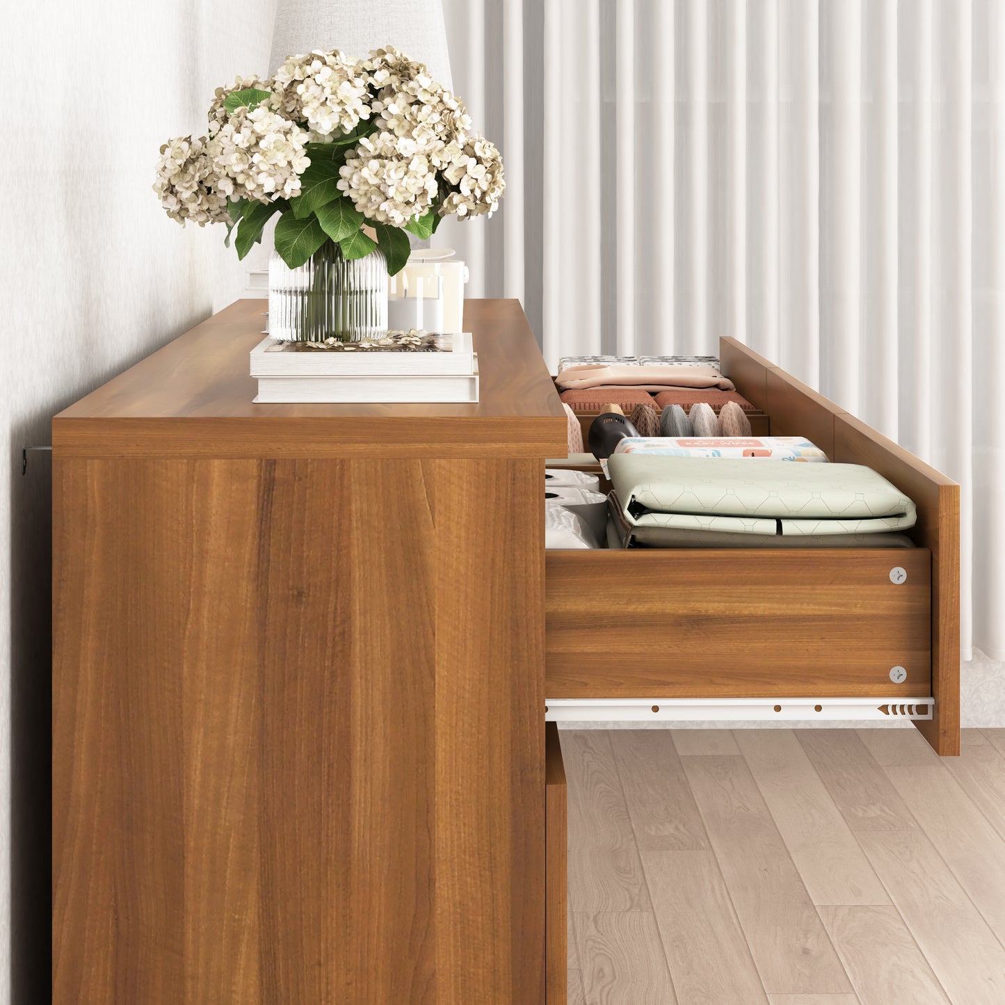 Wooden desk with a flower arrangement and folded clothes underneath a white curtain.